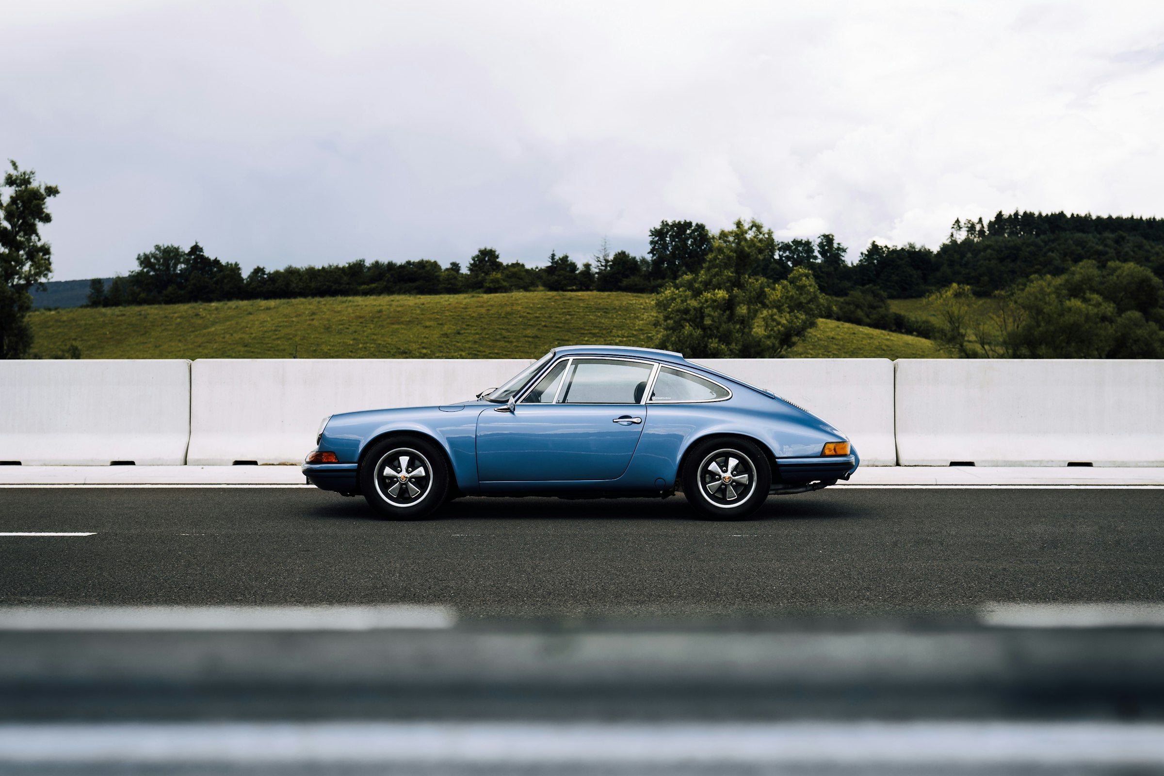 A blue classic 911 on an open road below a pale sky