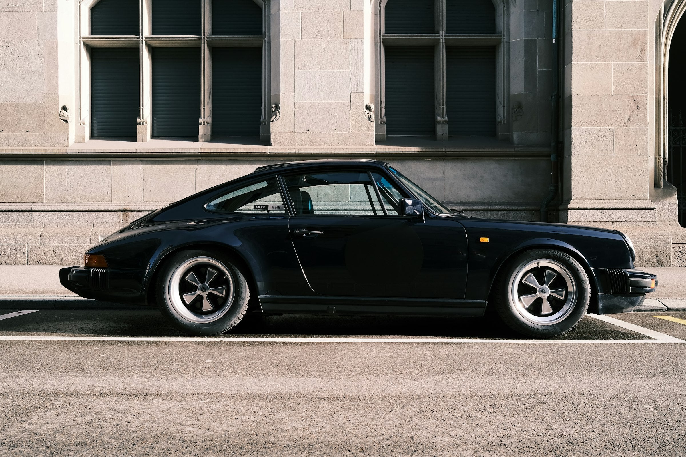 A black classic 911 parked in front of a pale stone facade