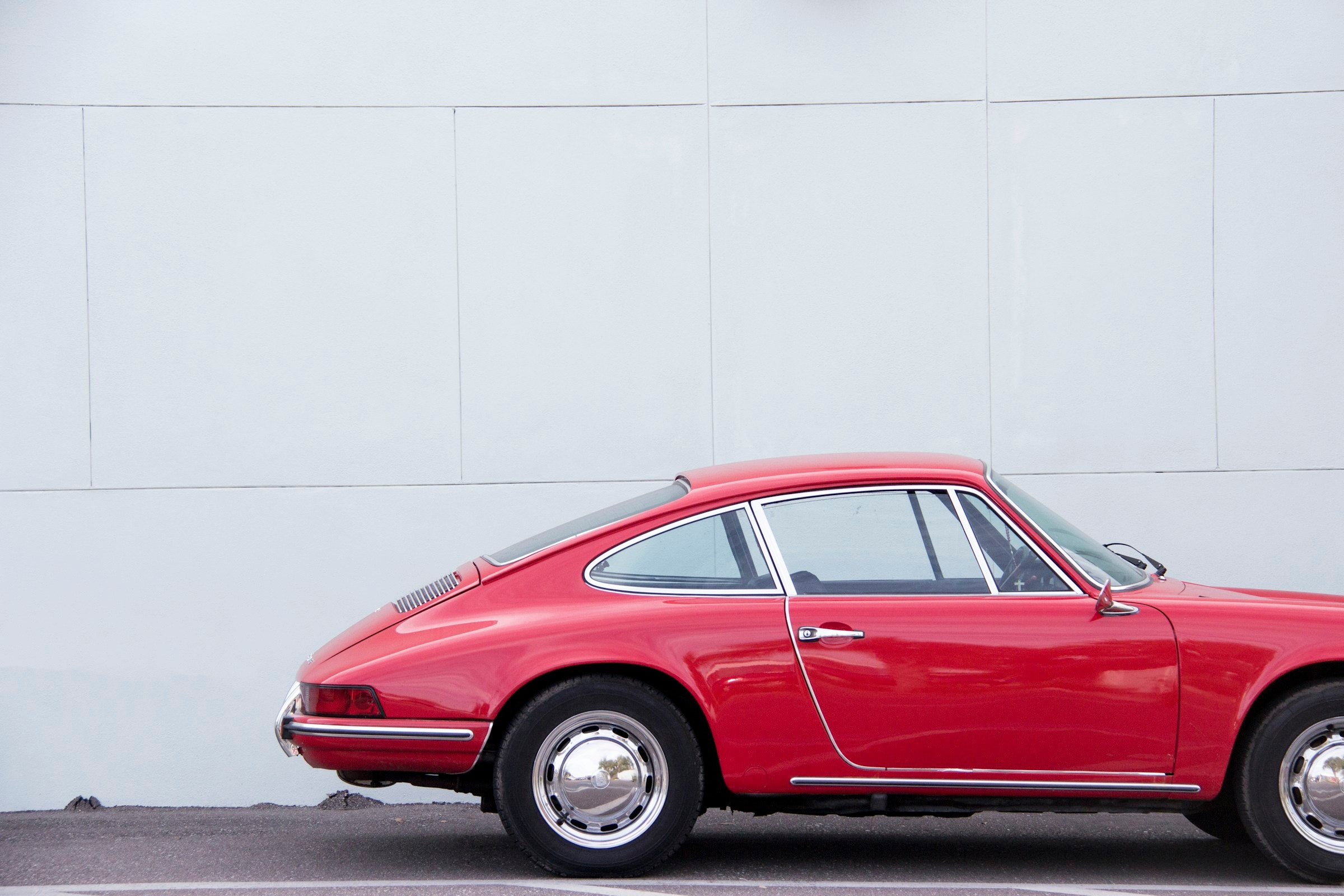 A red classic 911 in profile against a white wall